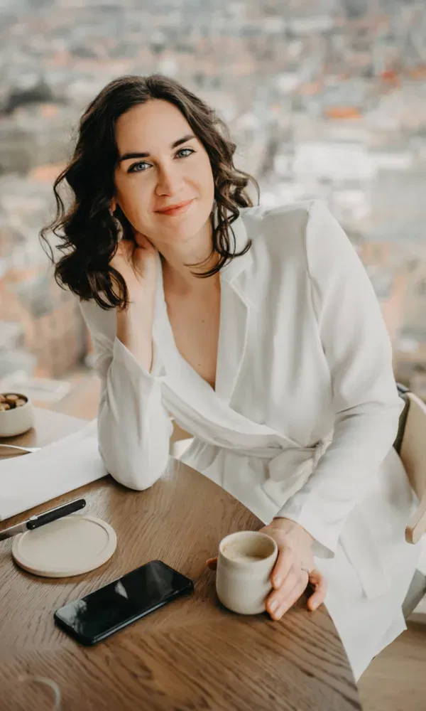 Eventzangeres Sarah Neyrinck in wit pak aan tafel, ze kijkt vrolijk de camera in.