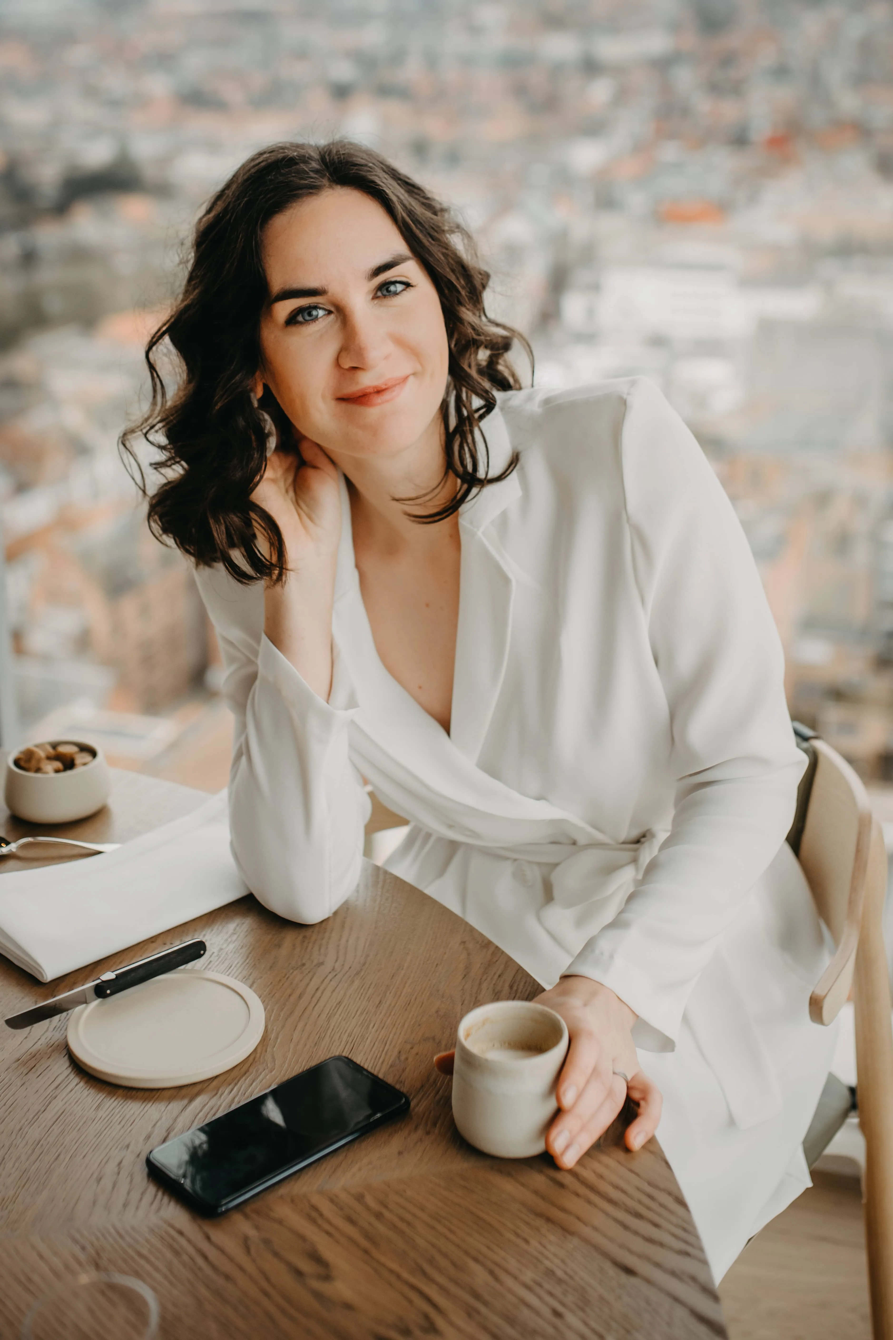 Eventzangeres Sarah Neyrinck in wit pak aan tafel, ze kijkt vrolijk de camera in.