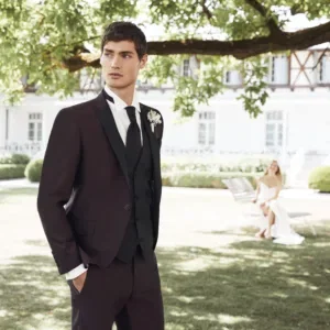 Bruidspaar in tuin, man op voorgrond in pak. Bruid op de achtergrond.