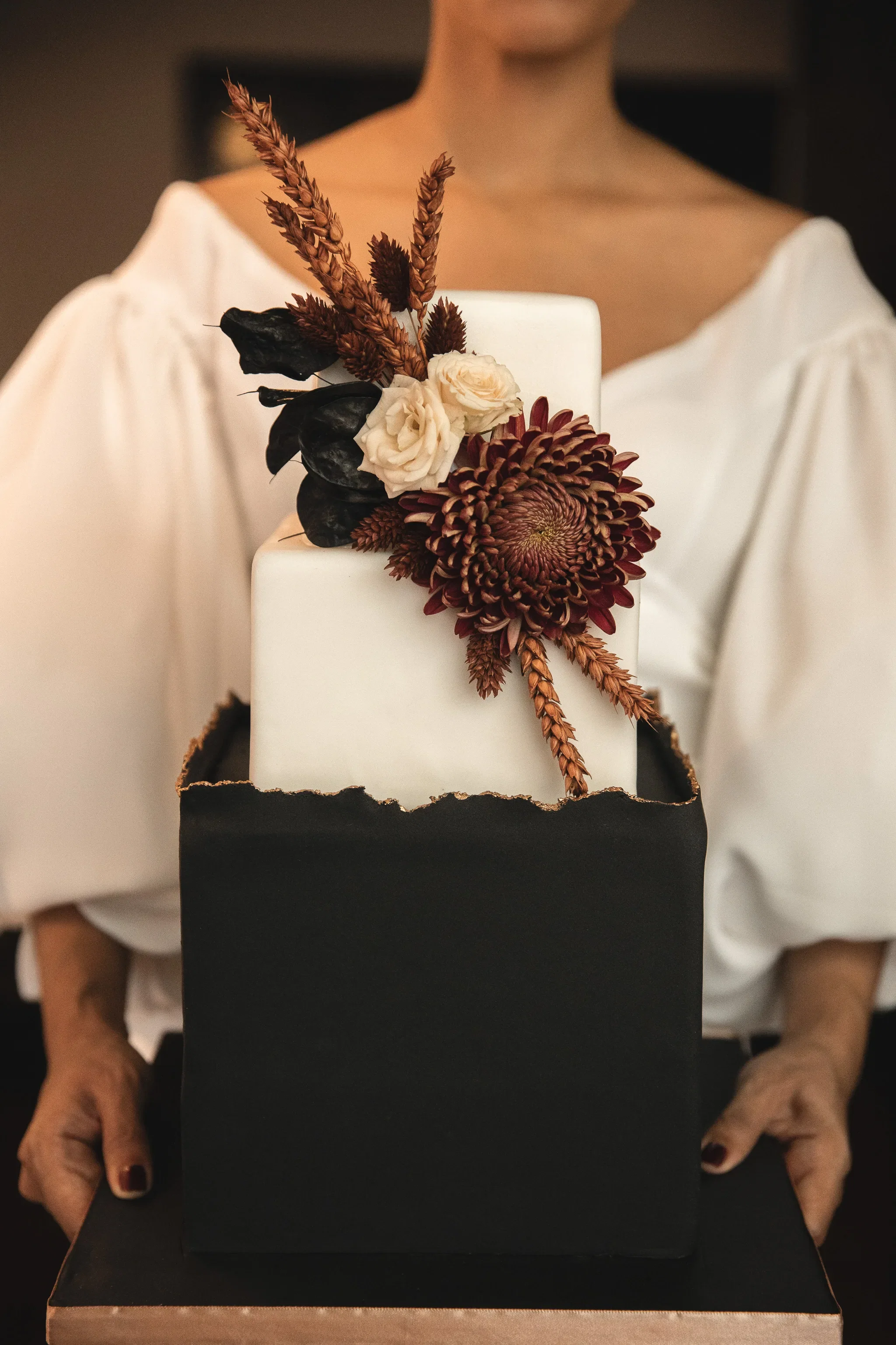 Bruid met vierkante bruidstaart waarvan de onderkant zwart en de bovenkant wit is. De taart is versiert met bloemen.
