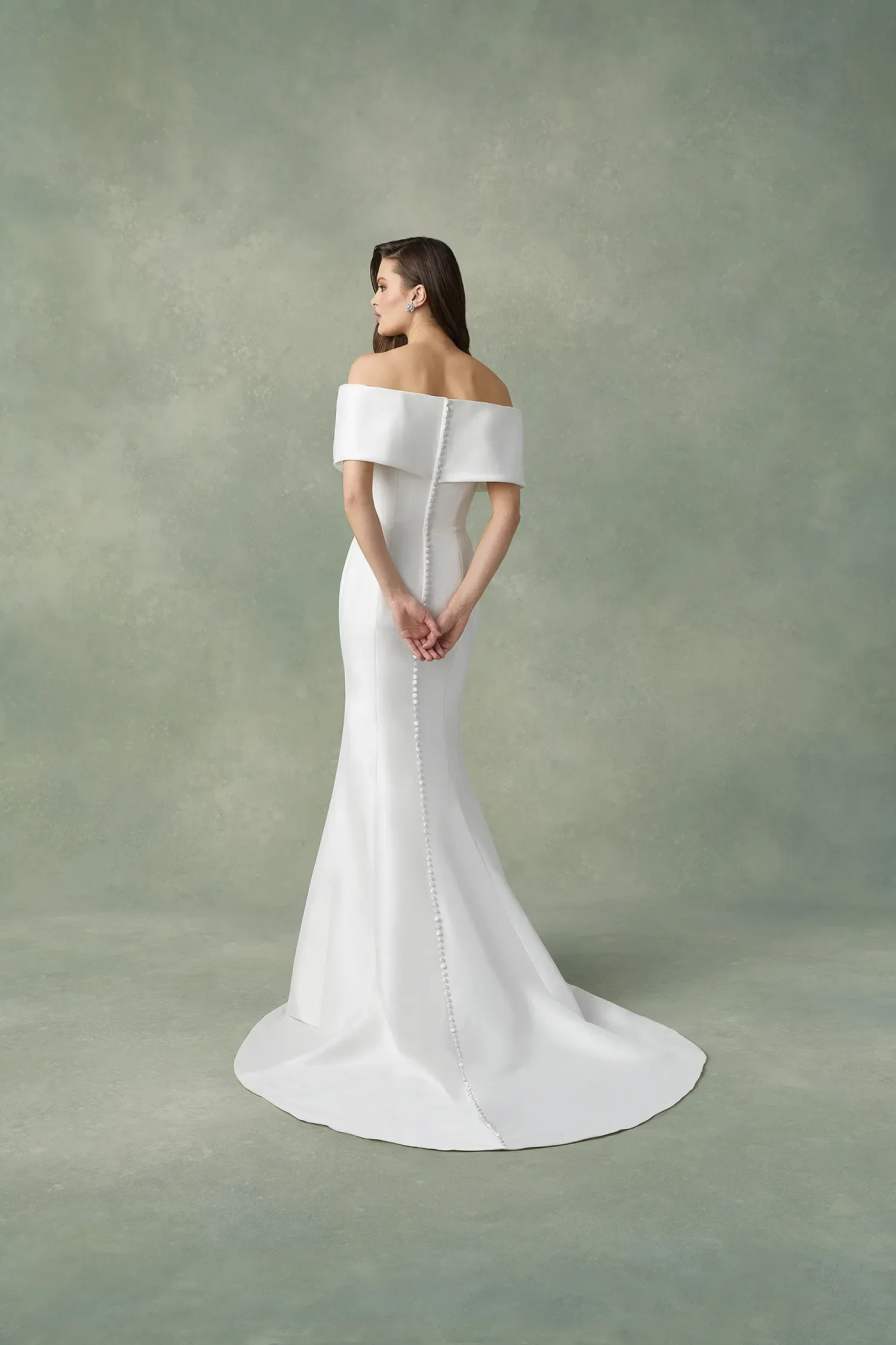 Bruid in off the shoulder trouwjurk, ze staat met de rug naar de camera. Knopen over de gehele achterkant.