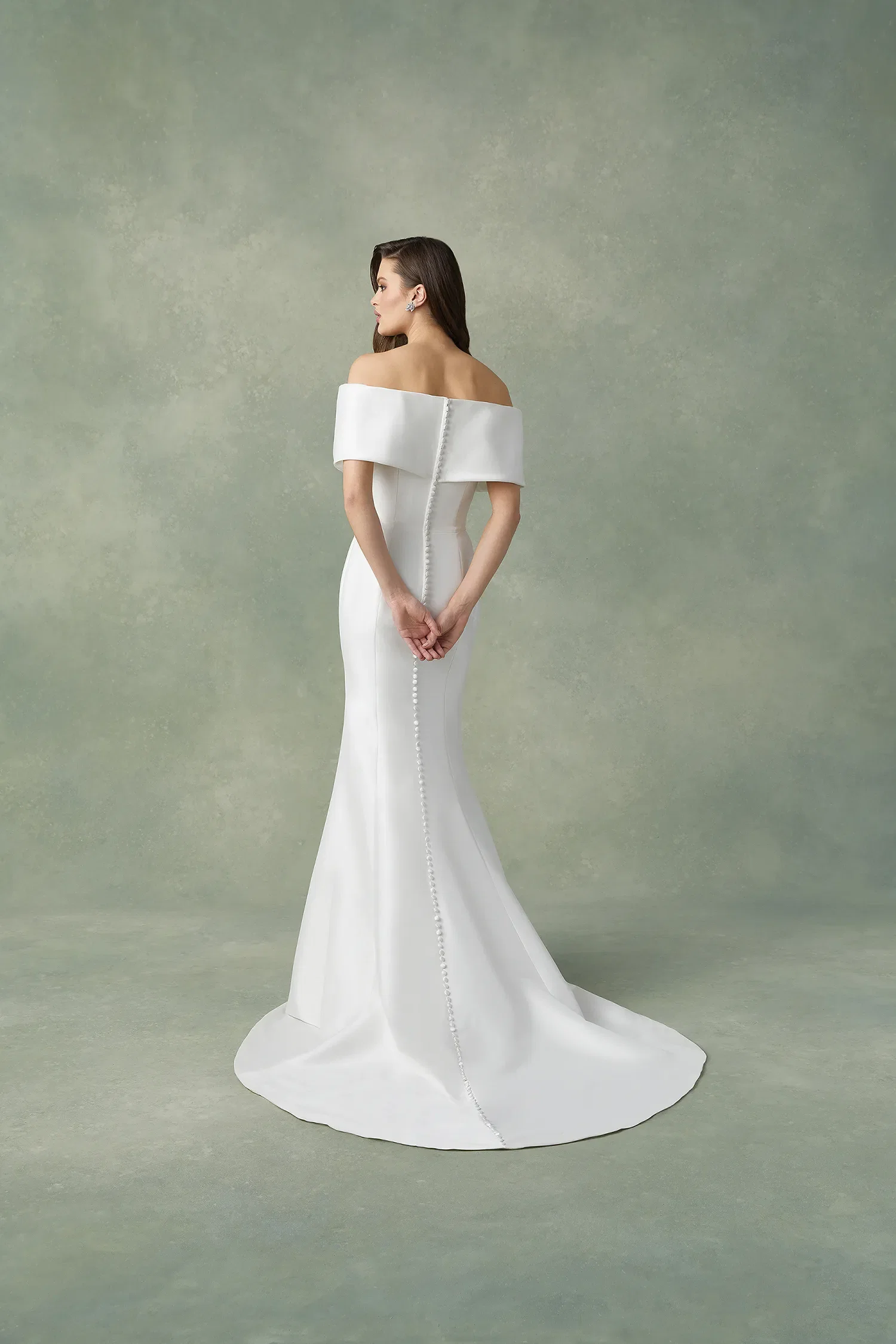 Bruid in off the shoulder trouwjurk, ze staat met de rug naar de camera. Knopen over de gehele achterkant.