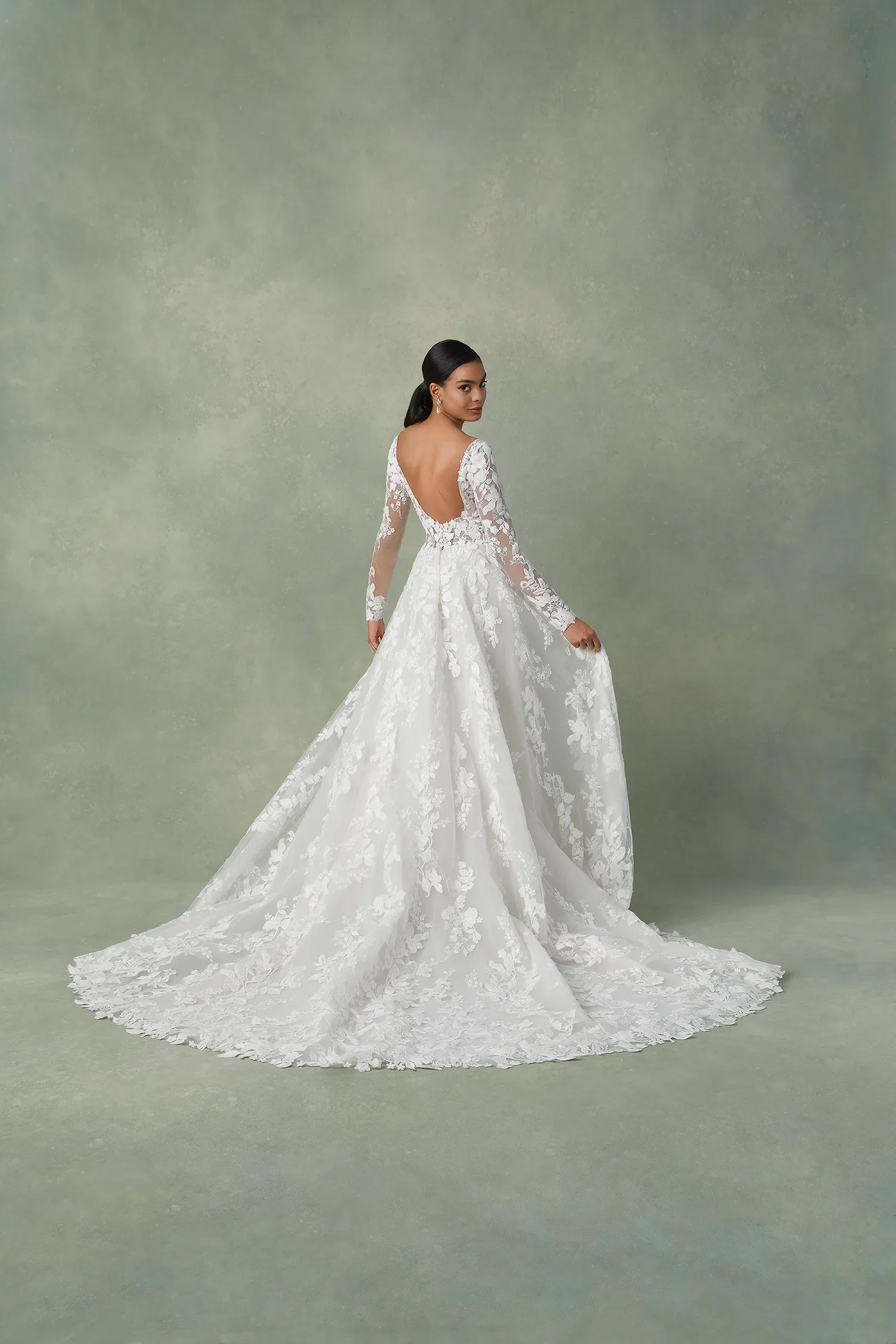 Bruid in een trouwjurk met bloemen en kant. Ze staat met haar rug naar de camera, de jurk heeft een open rug.