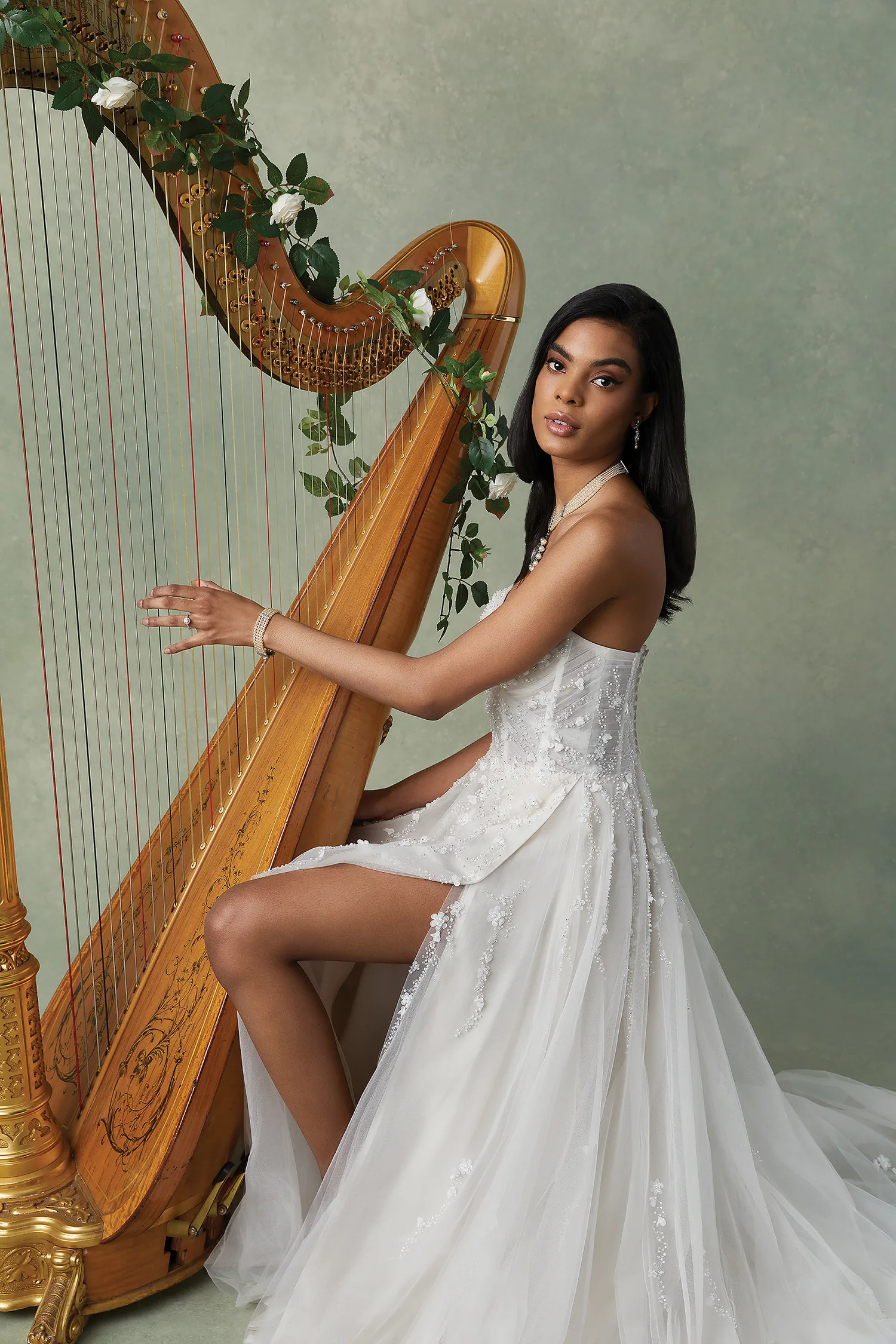 Bruid zittend bij een harp in trouwjurk met bloemen en tule.