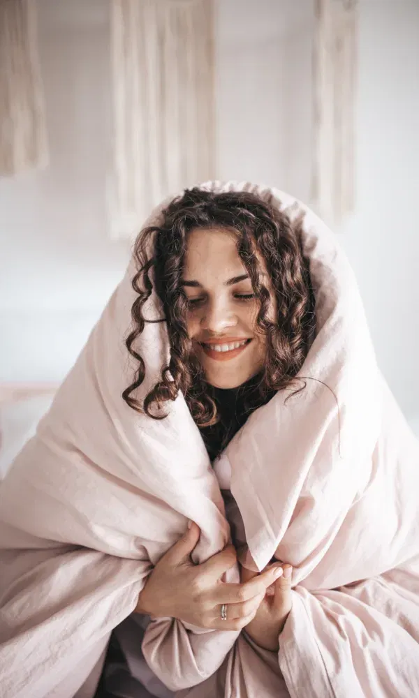 Vrouw kruipt onder roze dekbed en geniet van de ontspanning.