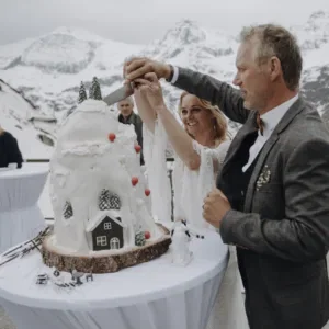 Bruidspaar snijdt taart aan voor besneeuwde bergen.