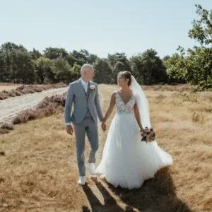 Bruidspaar in groen veld houden elkaars hand vast, 