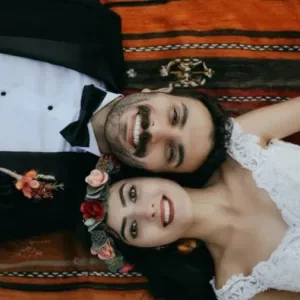 Bruid en bruidegom lachend op de grond met een bloemenkrans