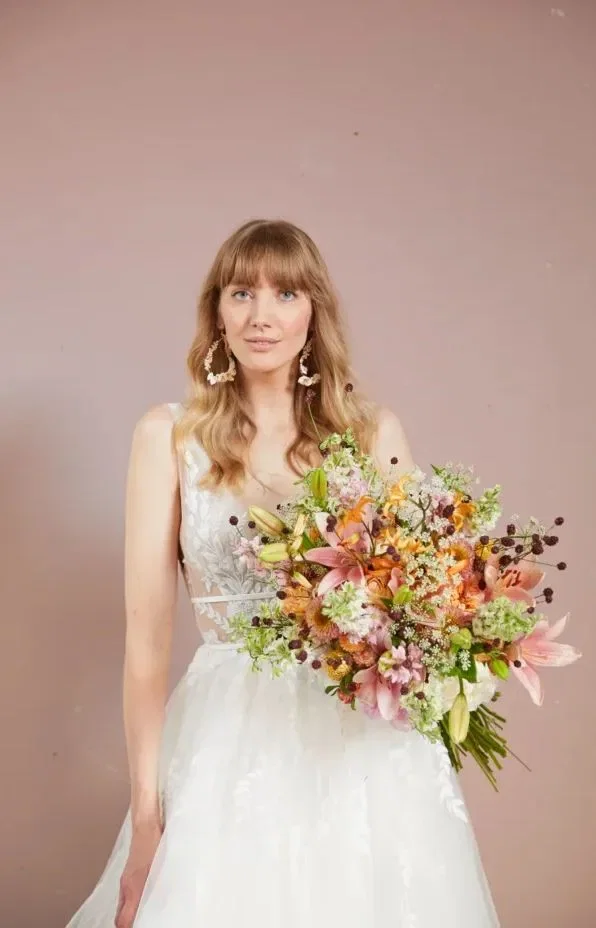 Bruid met witte jurk, bruidsboeket en grote schelp oorbellen