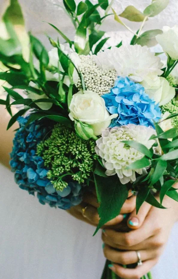 Een bruid houdt een bruidsboeket van met witte rozen en blauwe hortensia's