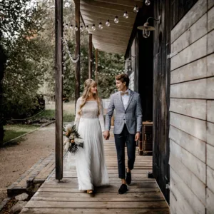 Bruidspaar loopt hand in hand naast houten hut.