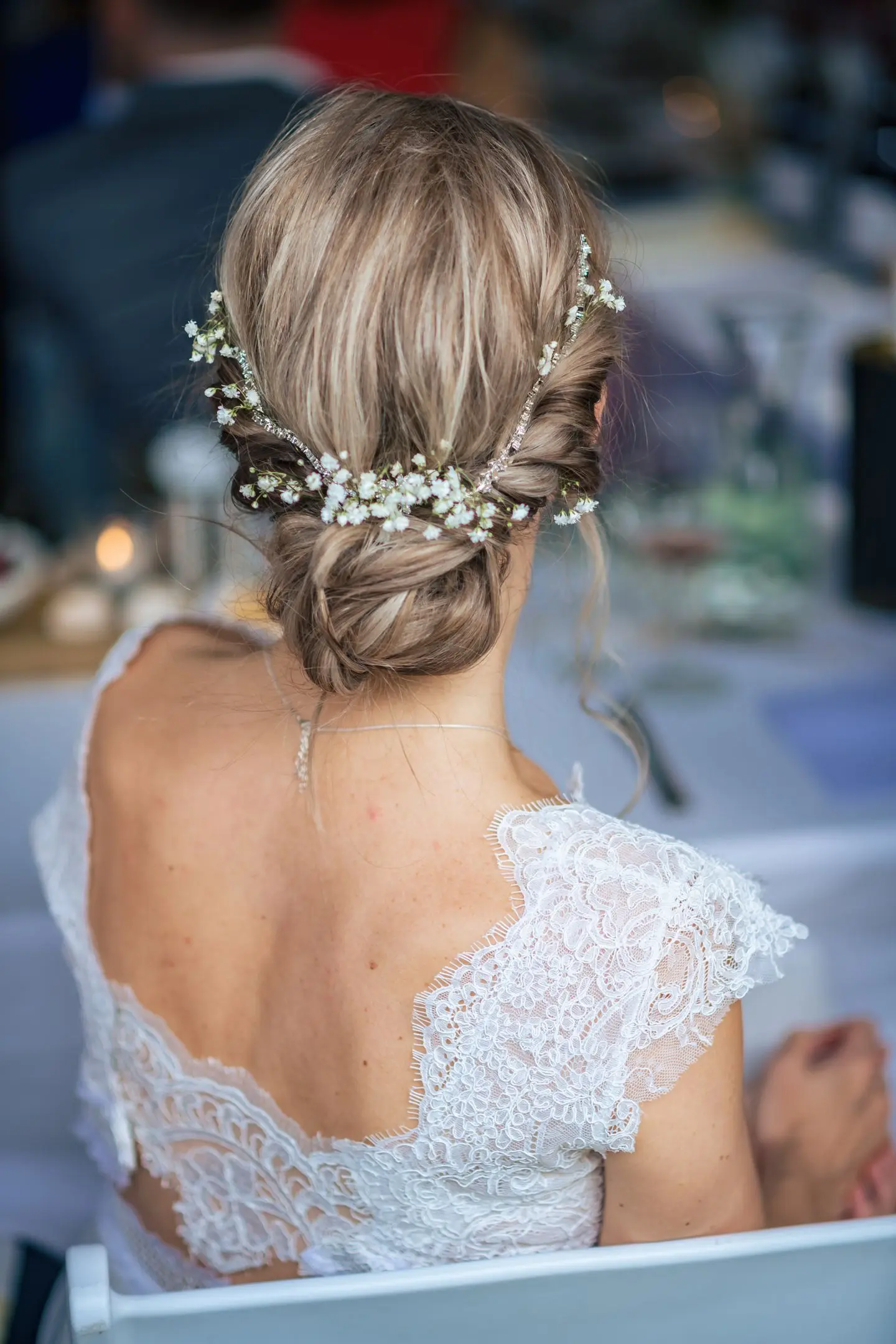 Bruid van de achterkant met lage knot en bloemetjes in het haar. Kanten bruidsjurk.