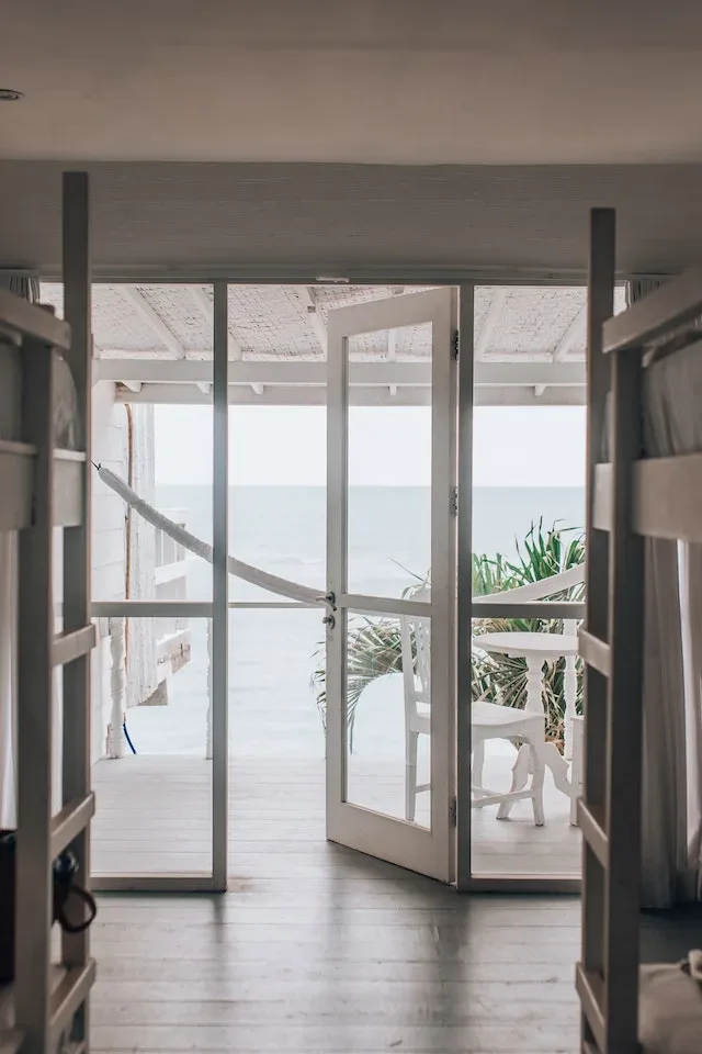 Open deuren van een strandhuis waardoor je naar buiten kijkt naar de zee.