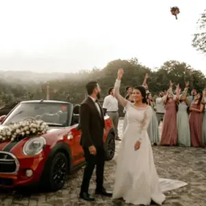 Bruid die haar bruidsboeket gooit, met een rode auto erachter.