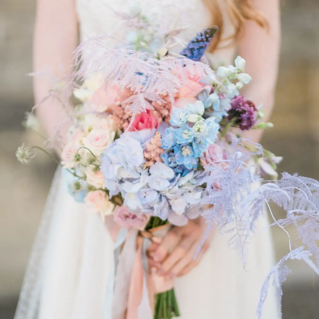 bruid met pastelkleurig bruidsboeket in de hand.