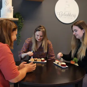 bruidstaartproeverij. drie vrouwen aan tafel, twee die proeven en de eigenaresse van de bakkerij.
