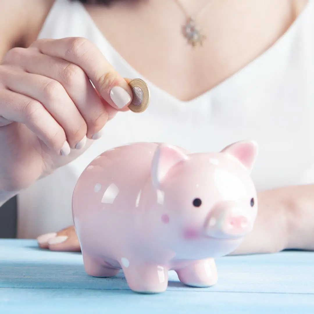 vrouw die een muntje in een roze spaarvarkentje stopt.