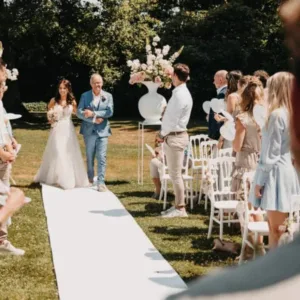 Buitenbruiloft. Bruid wordt wegegeven door vader in blauw pak.