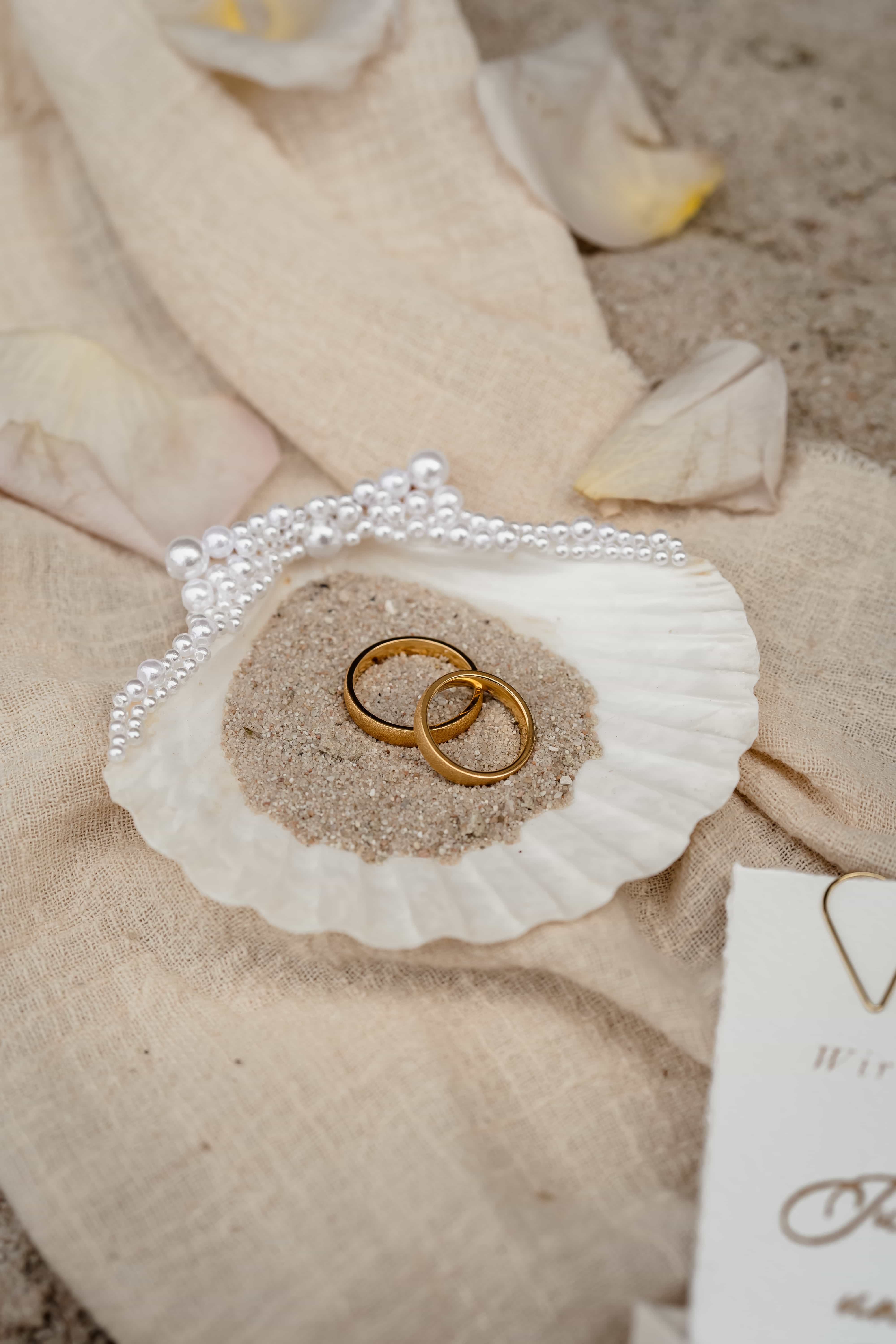Trouwringen op schelp in zand.