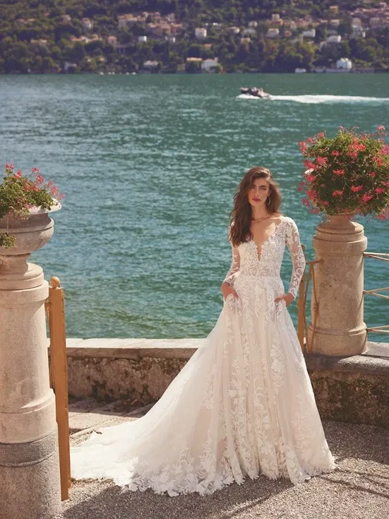 Bruid poseert met haar witte bruidsjurk met lange mouwen voor een azuurblauw meer